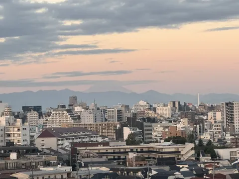 same window, hours later, and Fuji's still hanging low on the horizon while the sky goes peach over the rooftops. faint pink-grey lump but it's there.