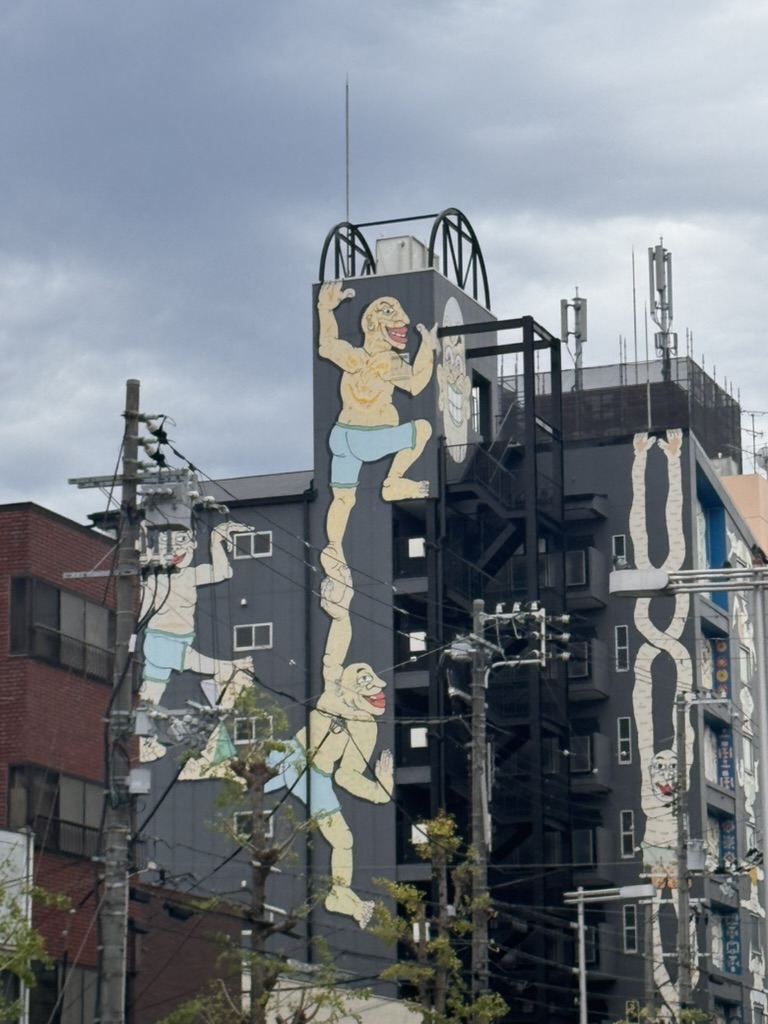 spotted this WILD street art near osaka's waterfront - those giant climbing figures are apparently a nod to the city's famous billiken statue