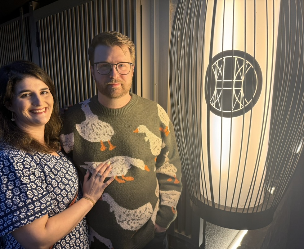 daniel and christina catching the last rays of golden hour outside a modern japanese restaurant in kyoto's shimogyo ward. loving dan's duck sweater against the geometric light fixtures.