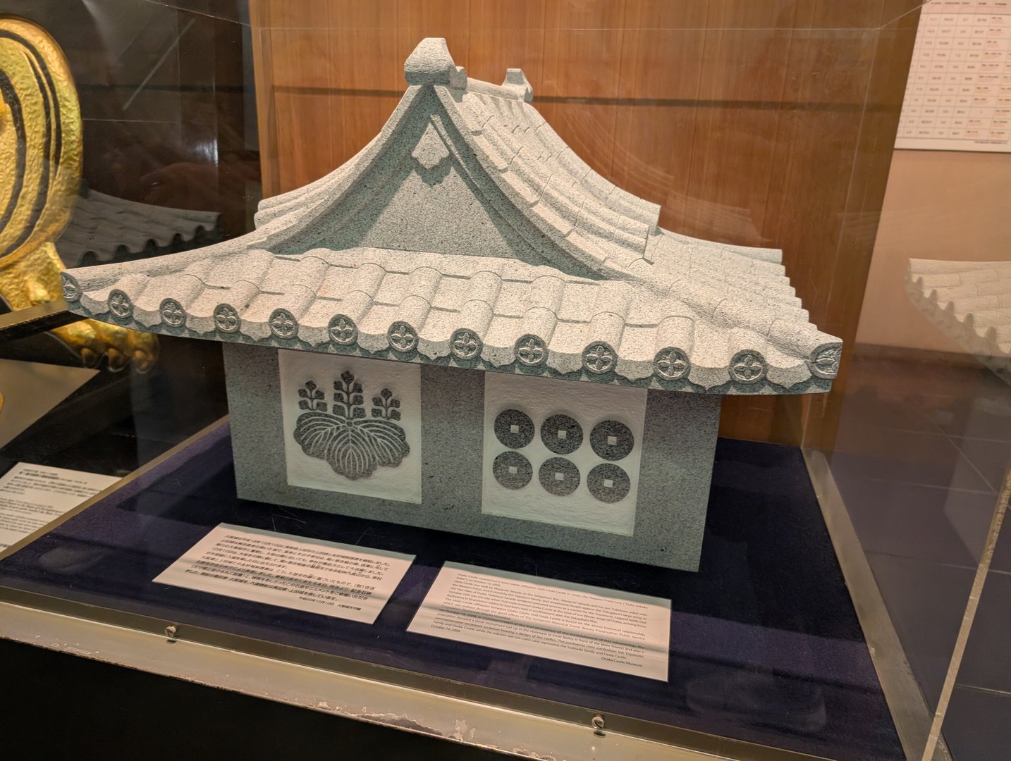 museum display at osaka castle showing a model roof tile with the tokugawa family crest and old japanese coins