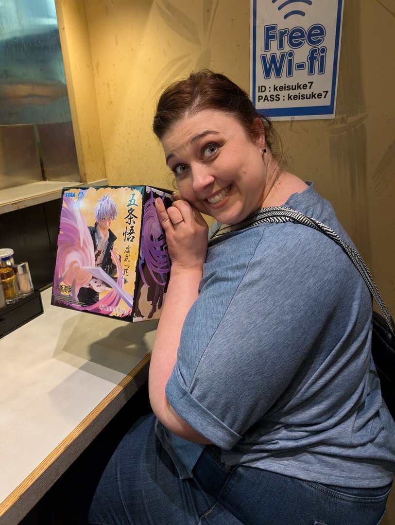 ashley showing off her anime merch find at a tiny ramen spot near akihabara. chuck's probably still trying to figure out how to use the ticket machine outside