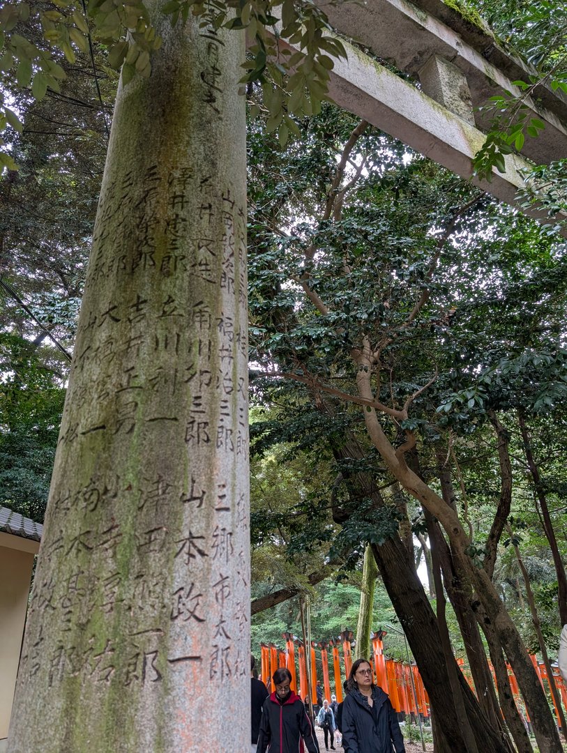 ancient kanji inscriptions on a stone pillar at fushimi inari, with the iconic orange torii gates peeking through in the background