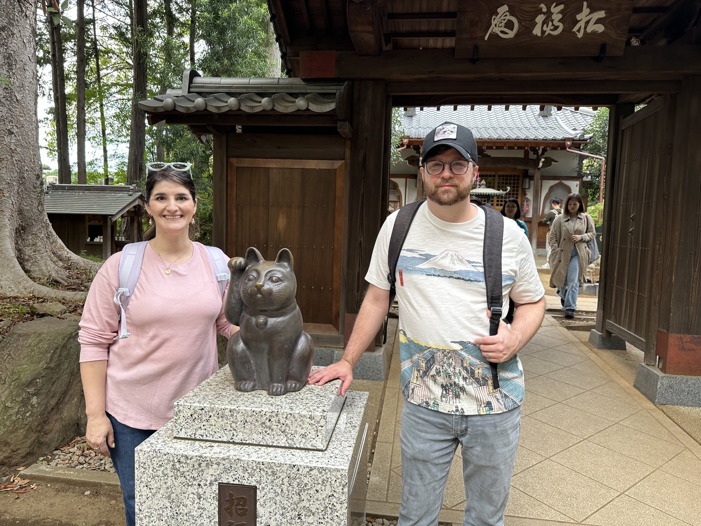 christina and dan with the lucky maneki-neko statue at gotokuji temple, where the beckoning cat legend began